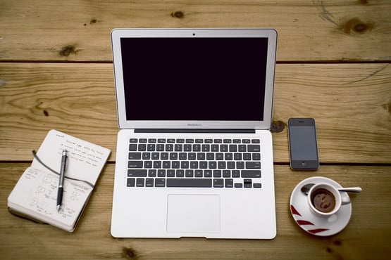 Apple MacBook, pad and paper, coffee cup, and smartphone on a table